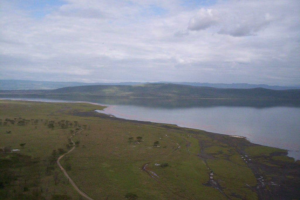 Panoramic view overlooking the open grasslands and shoreline of Lake Nakuru from the Baboon Cliff viewpoint.