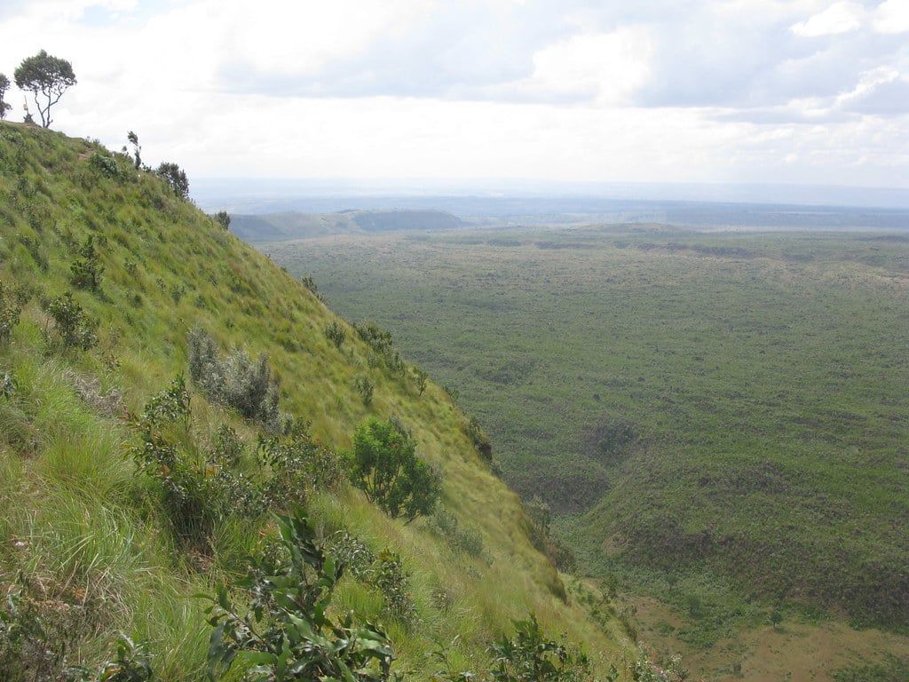 A view looking down from the steep, grassy rim across the wide expanse of Menengai Crater near Nakuru, Kenya.